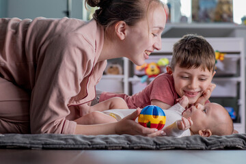 Happy mother playing with little children of different ages. Family at home.