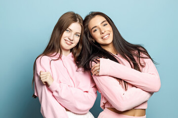 Two young beautiful smiling brunette hipster female in trendy pink clothes. Carefree women posing near blue wall in studio. Positive models having fun. Cheerful and happy. Close-up portrait