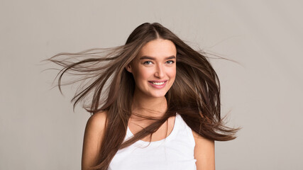 A young woman stands with her hair flowing in the wind. The wind gently tousles her hair as she looks off into the distance. Her hair is lifted and carried by the air