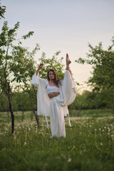 Obraz premium A woman in white poses near a tree with a cheerful smile, looking over her shoulder. This scene reflects the lighthearted and joyful interaction with the natural environment.