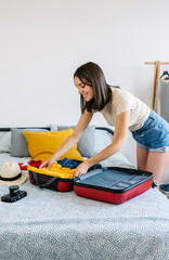 Vertical photo of happy young woman preparing summer suitcase before vacation. Female holiday maker...