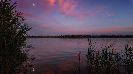 A serene sunset over a tranquil lake with rippled water, sky with soft clouds