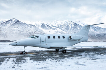 Naklejka premium White corporate airplane at winter airport apron on the background of high scenic snow capped mountains