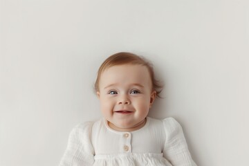 Adorable baby with light brown hair and blue eyes smiling, wearing a white dress, against a plain white background with ample copy space