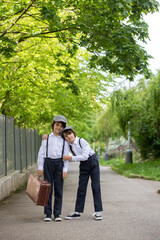 Fototapeta premium Sweet children in vintage clothing, hat, suspenders and white shirts, holding suitcase, running in the park
