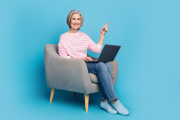 Full length photo of pensioner lady sit armchair laptop point empty space dressed stylish striped garment isolated on blue color background
