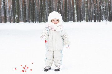 A cute baby in a snowy winter forest. Little girl having fun on winter day. Happy child in winter park.