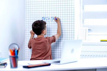 Rear view of young boy solving math problems on white board.