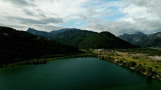 Drone view over a lake with green majestic mountains and blue sky with clouds in Le Broc, France