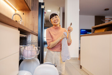 A japanese housewife unloading dishwasher and wiping utensils at home.