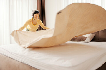 A worthy japanese woman making her bed in a bedroom.
