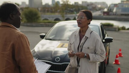 Medium of smiling African American woman in her twenties having conversation and shaking hands with instructor after completing driving course and obtaining license