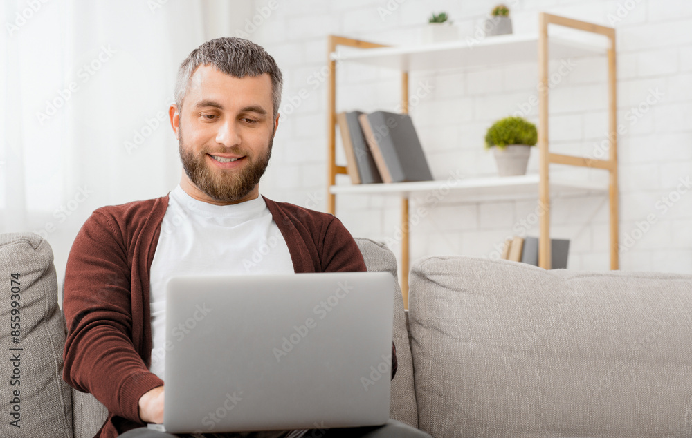 Aufkleber a man is seated comfortably on a couch, engrossed in his laptop screen. he appears focused as he typ
