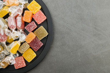 Assorted jelly candies on black tray, top view.