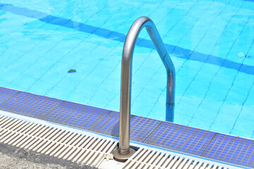 Closeup of Stainless Steel Handrail or Grab bars ladder in the clear blue swimming pool, Concept for convenience in entering the swimming pool at Thailand.
