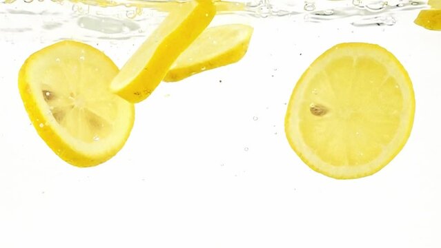 Refreshing essence of a lemon being sliced and falling into water in slow motion on white background. Yellow citrus fruit making splashes and bubbles in liquid. Healthy qualities of vegetarian food