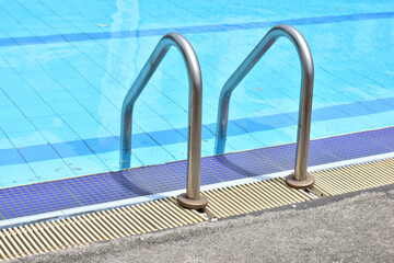 Closeup of Stainless Steel Handrail or Grab bars ladder in the clear blue swimming pool, Concept for convenience in entering the swimming pool at Thailand.