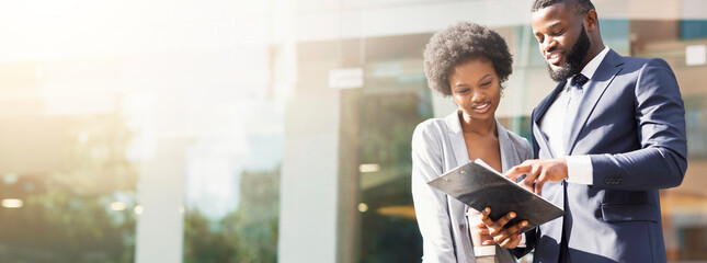 Happy couple of african american business partners working while standing outdoors, discussing new...