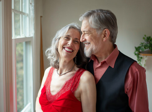 Coppia felice di uomini anziani abbracciati vicini alla finestra, uomo e donna, che si amano e sorridono. Vicini, lei con abito rosso e lui abito elegante.