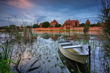 Castle of theTeutonic Order in Malbork by the Nogat river at sunset.