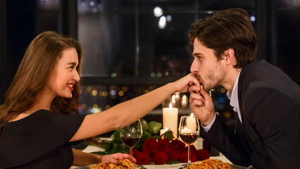 Handsome man in suit kissing hand of attractive woman wearing dress in restaurant during romantic...