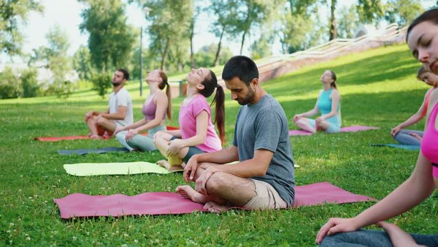 Outdoor yoga class in park with group practicing meditation and breathing exercises. Concept of relaxation and mindfulness