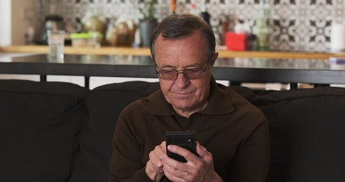 Elderly caucasian male person typing message on smartphone screen. At home, living room. Pattern, space for text