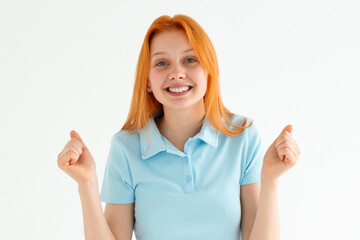 Portrait of ecstatic woman 20s wearing blue t-shirt clenching fist like rejoicing victory or triumph isolated over white background