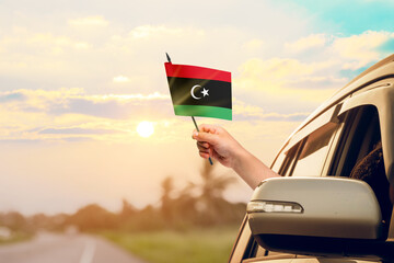 Waving the Libya flag against the sunrise or sunset from a car driving along a country road....