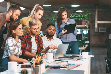 Several individuals standing around a table, viewing content on a laptop screen with focused expressions.