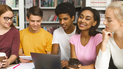 International Team Of College Students Studying At Library, having fun while working with laptop