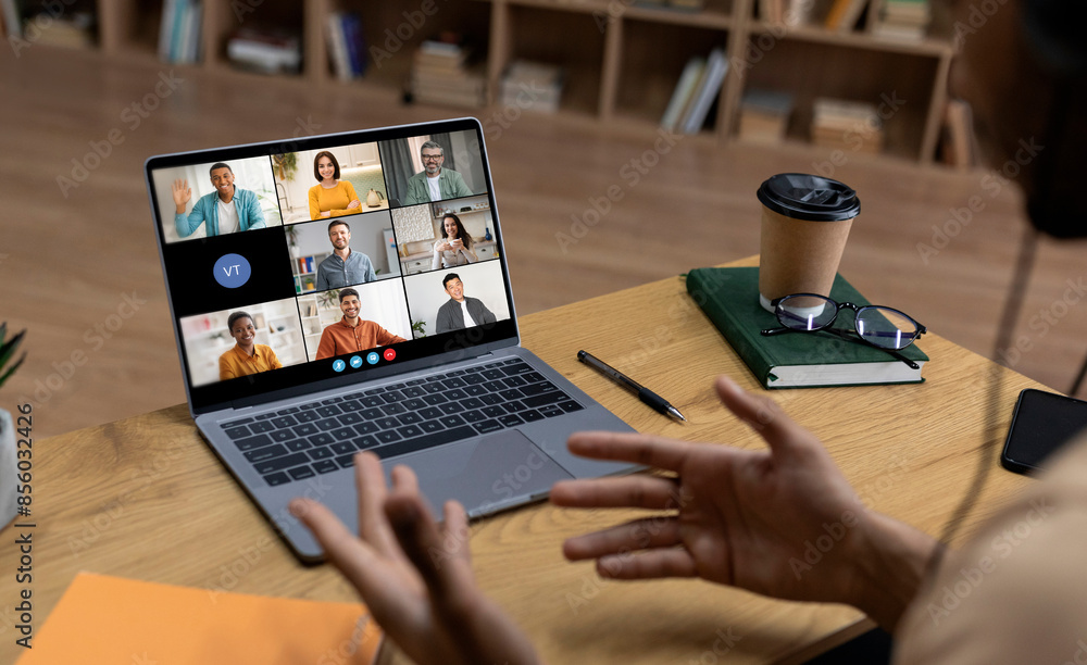 Poster a person is sitting at a desk in front of a laptop computer, participating in a video conference cal