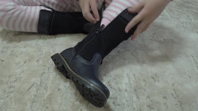 put on boots with a zipper, the little girl puts on her boots and fastens the zipper