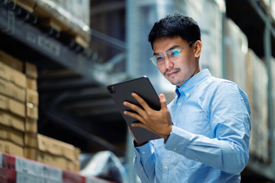 warehouse worker in a blue security suit uses a digital tablet to inspect inventory in a large warehouse. Distribution Center. Logistics and export of business.