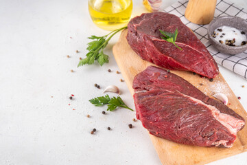 Raw meat steaks ready for cooking grilling. Two beef steaks on cutting board, with herbs, spices, olive oil, on cooking table top view copy space