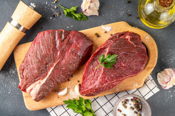 Raw meat steaks ready for cooking grilling. Two beef steaks on cutting board, with herbs, spices, olive oil, on cooking table top view copy space