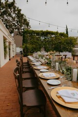Outdoor dining setup with a long table decorated with plates, glasses and candles