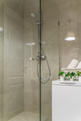 modern bathroom design with light-colored tiles, white furniture and a white toilet bowl. Glass shower cabin with sliding doors