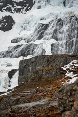 magnificent Dynjandi waterfall in Iceland is covered in a stunning blanket of ice and snow, creating a truly breathtaking sight, a hiker in a red jacket enjoying the scenery