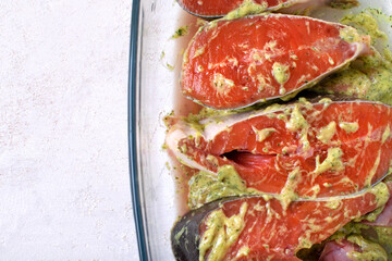 Pink salmon steaks in creamy sauce with herbs in the glass dish prepared for being roasted in the oven