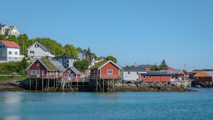 Fototapeta premium A scenic view of Reine, Lofoten, Norway, waters edge, with a clear blue sky and calm waters in the background.