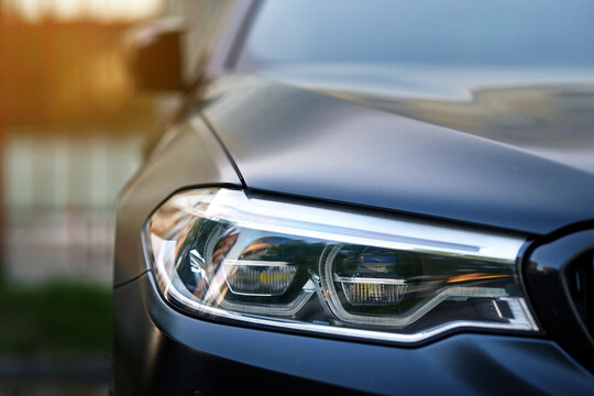 Minsk, Belarus. May 3, 2024. Headlight of modern black sports car BMW M5 F90 Competition at the parking lot. LED adaptive headlights closeup.