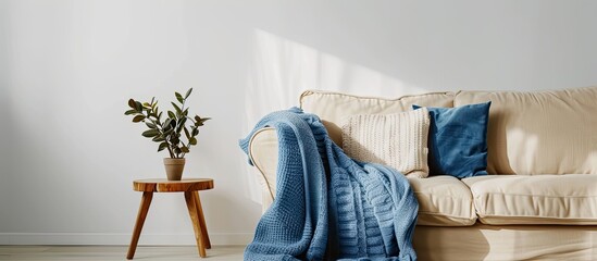 Beige sofa with a blue blanket against white empty wall, copy space in simple living room.