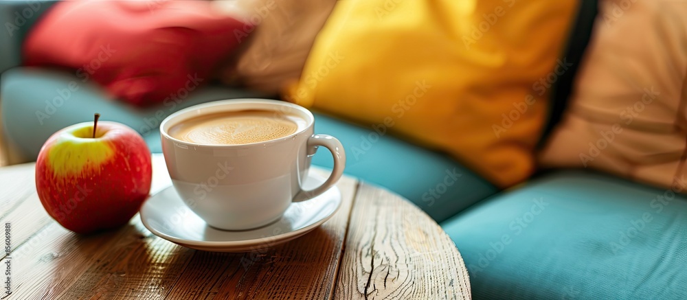 Poster Mug of coffee and apple on wooden table with colorful couch in the house. with copy space image. Place for adding text or design