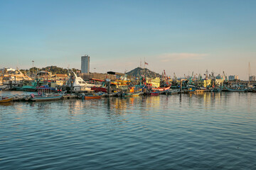 Fototapeta premium A panoramic view of a harbor filled with docked fishing boats, with the setting sun casting a warm glow on the water and boats.