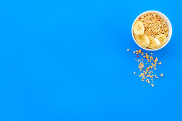 Healthy granola with banana in bowl for colorful breakfast on blue background top view mock-up