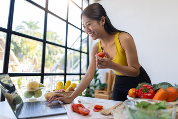Beautiful Asian influencer woman making vegetable salad at home. Fitness influencer on social media online showing tomato for healthy eating. Vlogging and blogging online, weight loss and dieting.