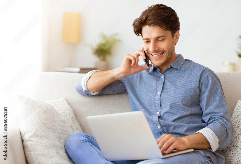 Poster a man sits on a couch, smiling while talking on his phone and working on his laptop.