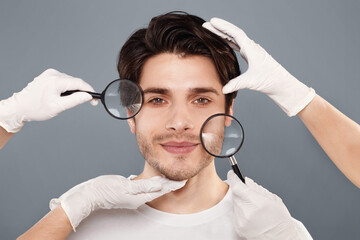 Rejuvenation and skin care. Face of young handsome man with beautician's hands and magnifiers