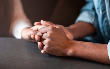 Two individuals are seated at a table, holding hands. Their interlocked fingers convey a sense of connection and intimacy. The table is simple, adding to the focus on the human interaction.